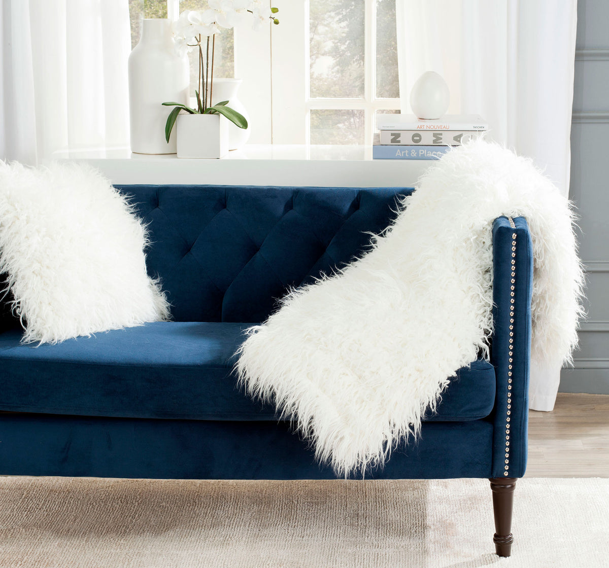 A fluffy white faux fur throw drapes over a navy sofa arm, its long pile cascading onto the seat. || THR704A-5060 || front_angle_room
