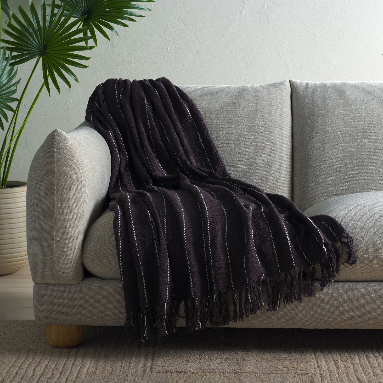A charcoal gray cotton throw drapes over the sofa, adding cozy texture, white stripes, and fringe. || THR858A-5070 || front_angle_room