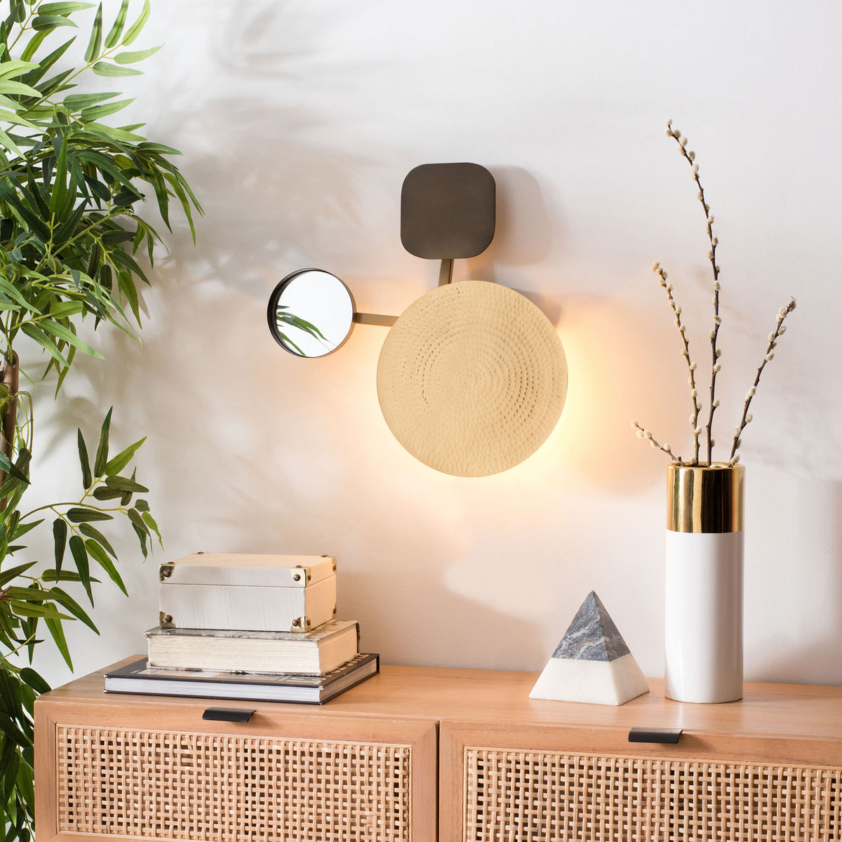 Warm backlighting frames the hammered gold-tone disk and small mirror above a console
