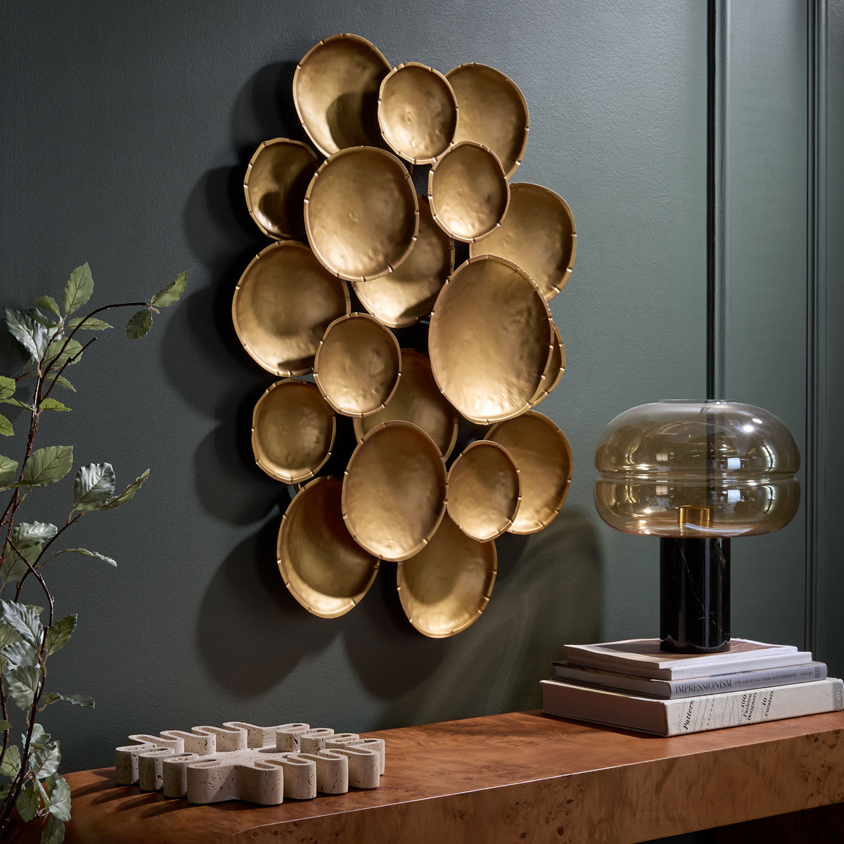 Layered gold discs bring warm metallic texture to a dark accent wall above a wood console