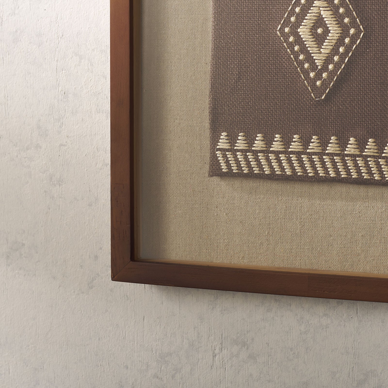 A warm wood frame borders textured beige linen and intricate brown-and-cream textile motifs. || WLA1902A || detail_room