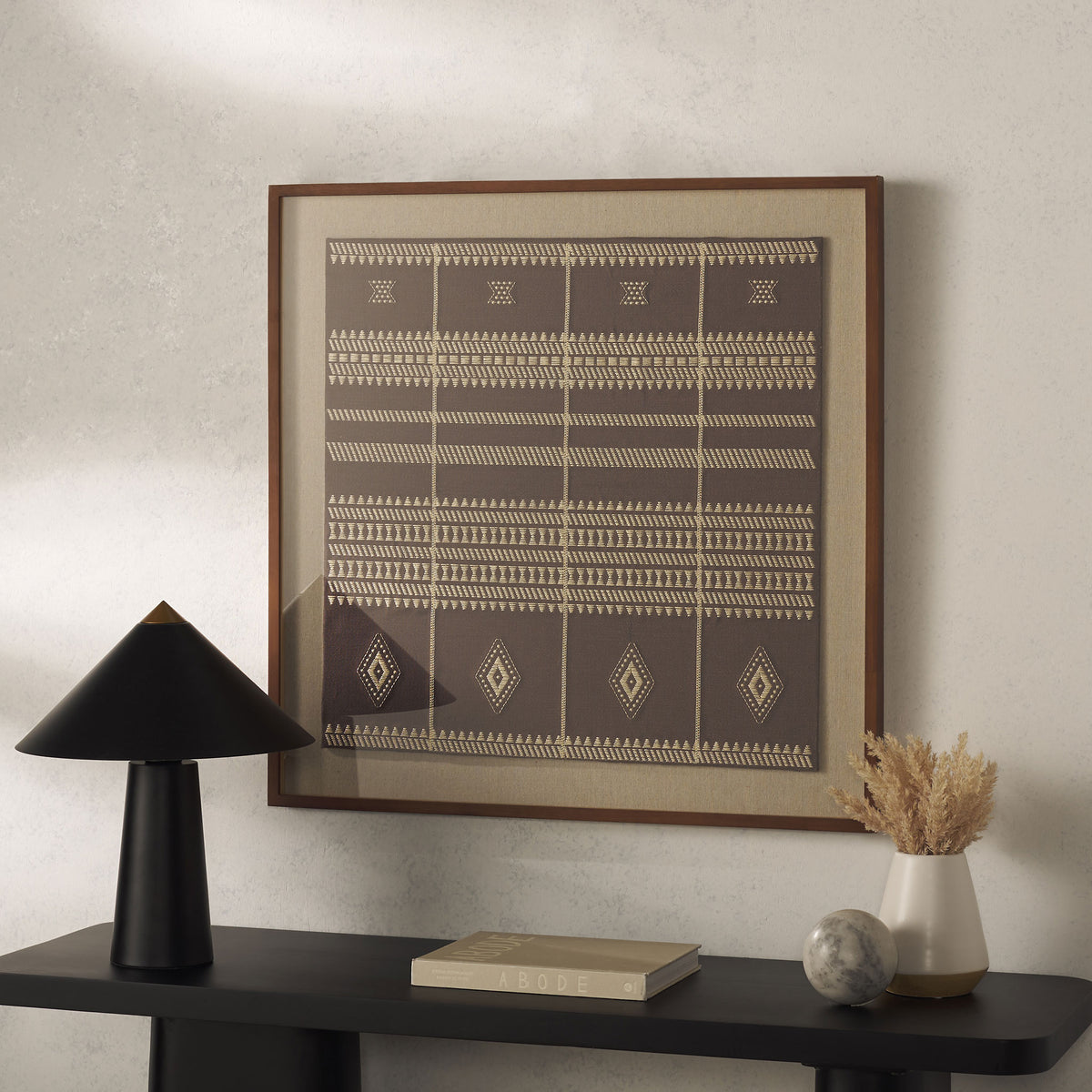 Warm brown textile art with cream stripes and diamonds creates a bold accent above a black console.