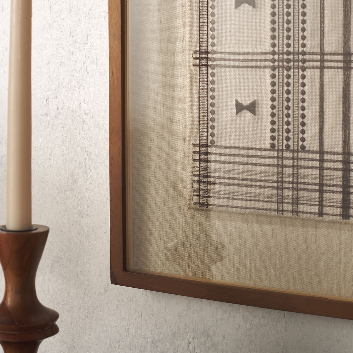Fine brown linework and dotted bands contrast with textured cream fabric and a warm wood frame