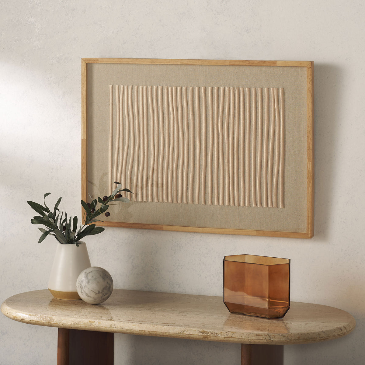 A natural wood frame and raised beige embroidery give this wall art understated texture above an accent table