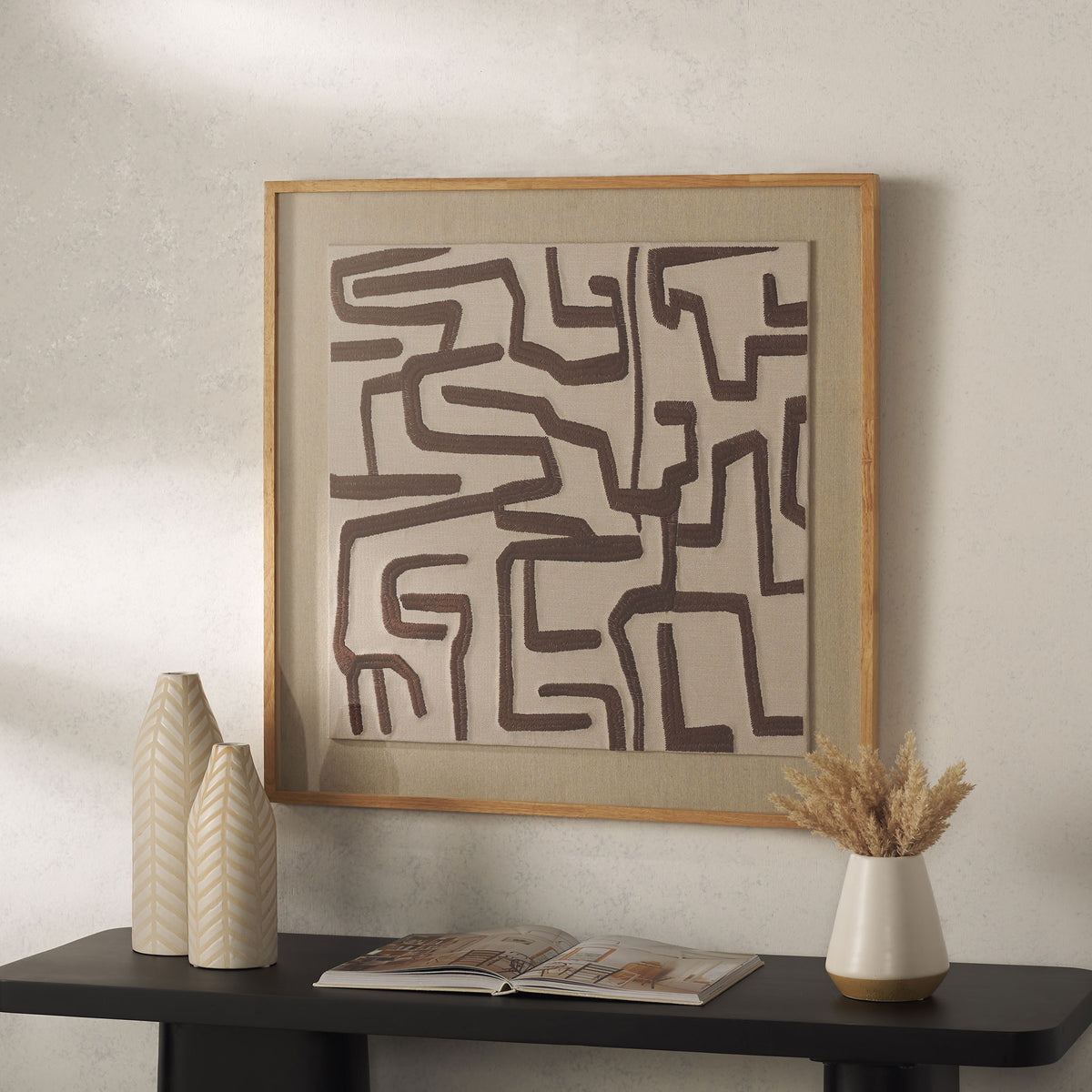 Ivory textile art with chocolate brown geometric lines and a light wood frame adds warmth above a console