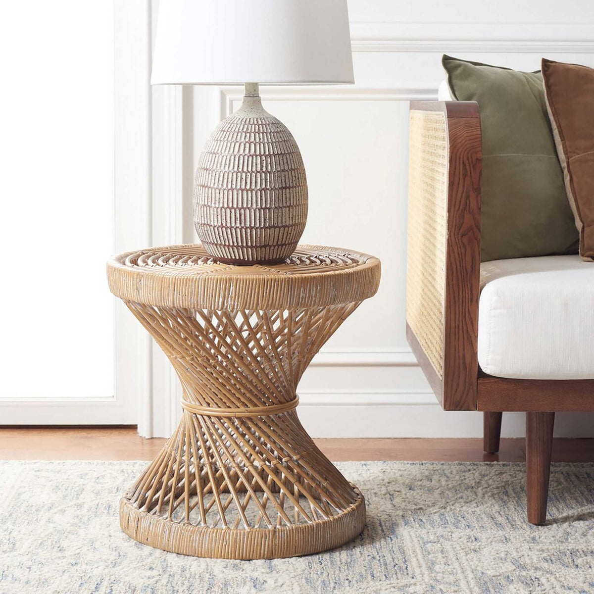 Sculptural woven rattan accent table holds a lamp beside a sofa