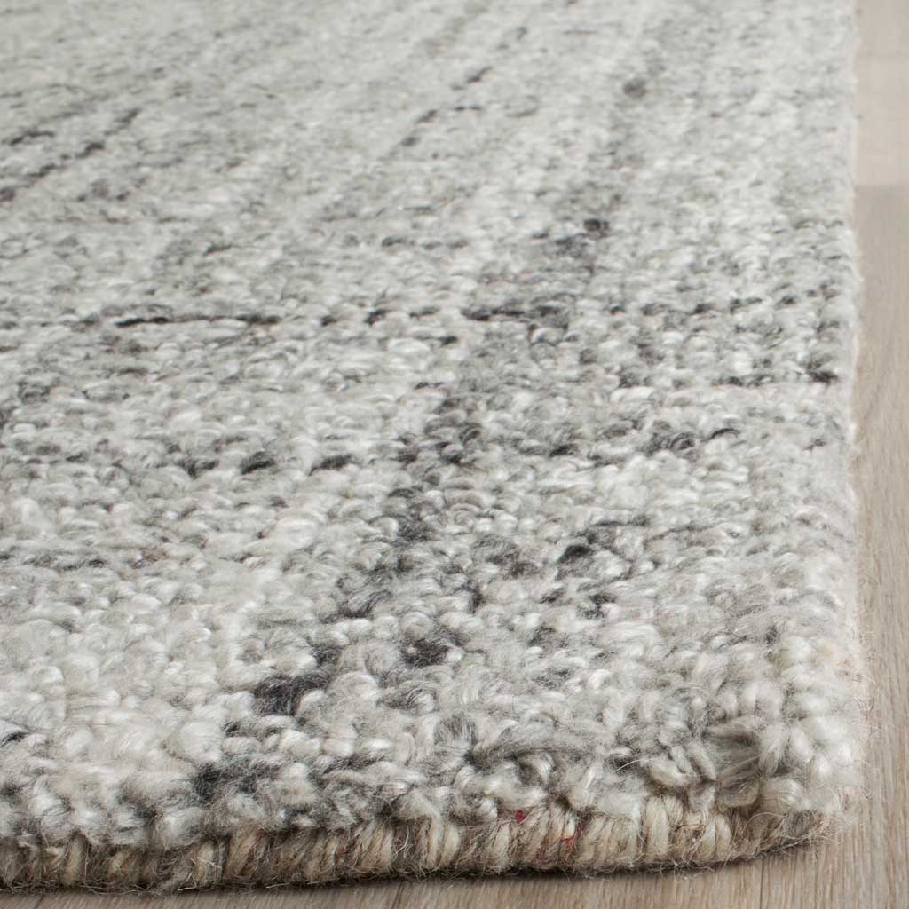 Thick, tufted gray fibers are flecked with black along the rug's finished edge