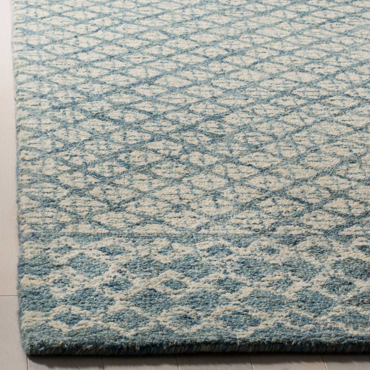 A neatly bound edge frames plush wool pile with layered blue motifs on an ivory ground.