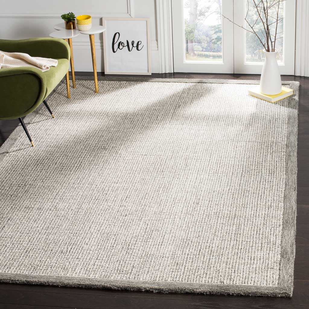 Muted sage trim outlines a light ivory wool rug with fine, irregular markings.