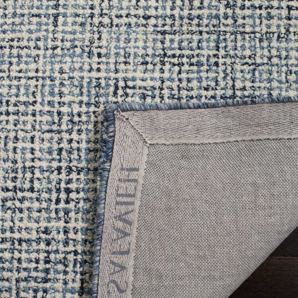 Bound navy edging and woven fabric backing finish the blue-flecked ivory rug.