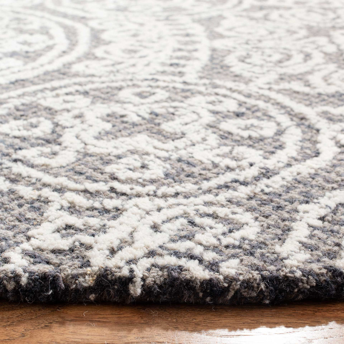 Plush hand-tufted wool pile gives ivory floral scrollwork rich texture against a gray ground.