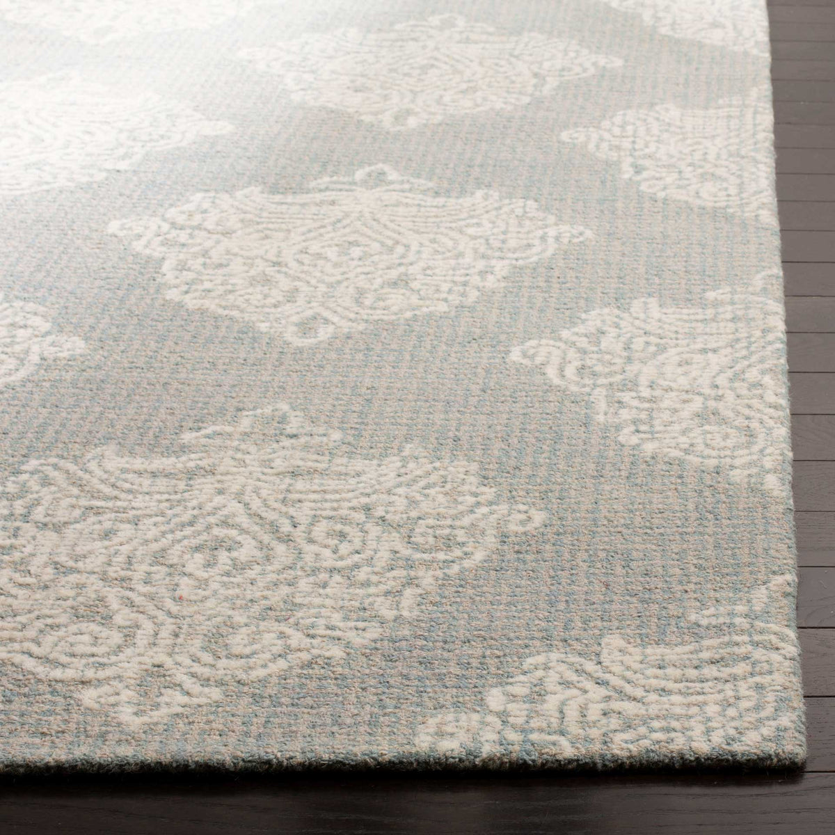Raised ivory damask motifs stand out against the aqua wool pile and neatly finished rug edge.