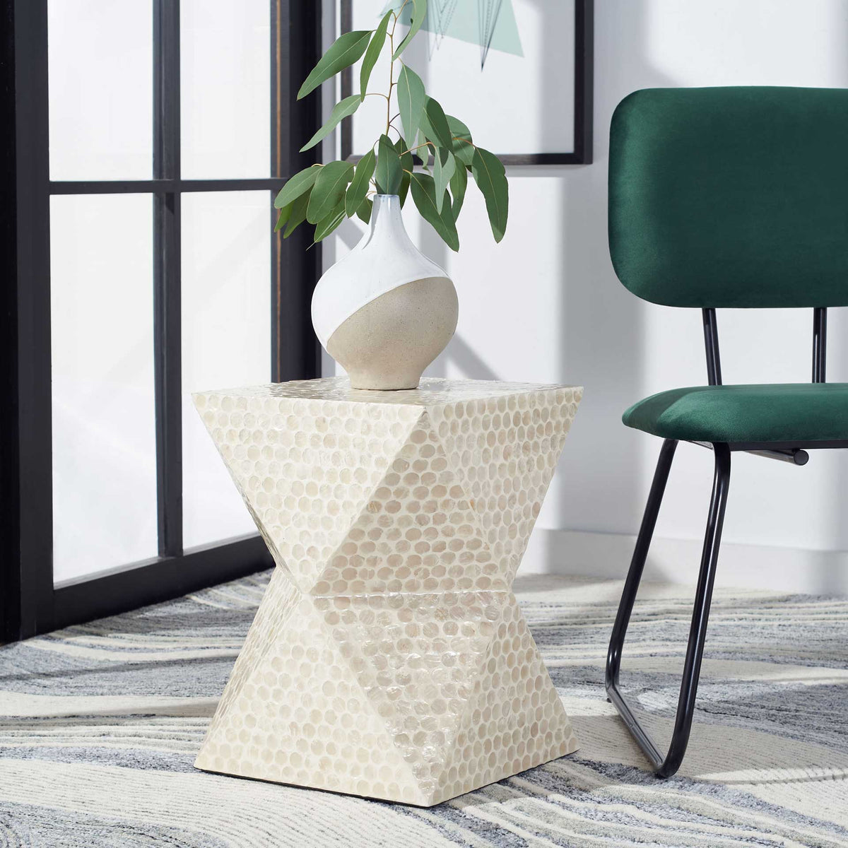 A luminous capiz shell accent table brings sculptural texture beside a green chair.