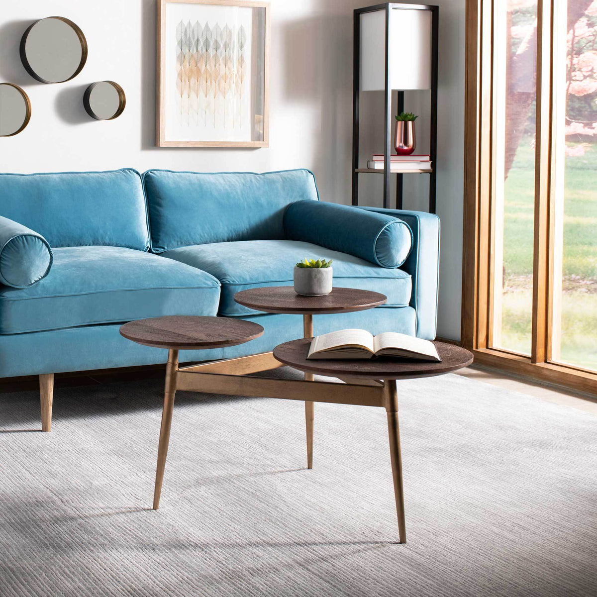 Three staggered circular tops hold books and decor beside the sofa on slender gold-tone legs.