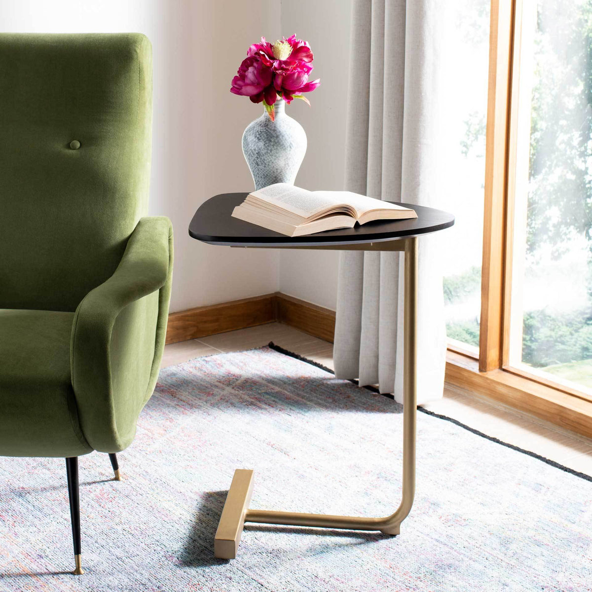 An oval black tabletop holds a book and vase beside a chair, supported by a slim gold metal frame.