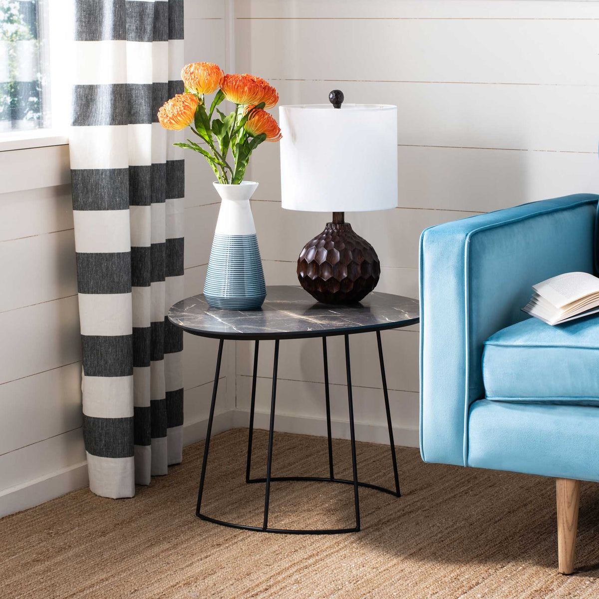 A veined dark tabletop holds a vase and lamp on an airy black metal base.