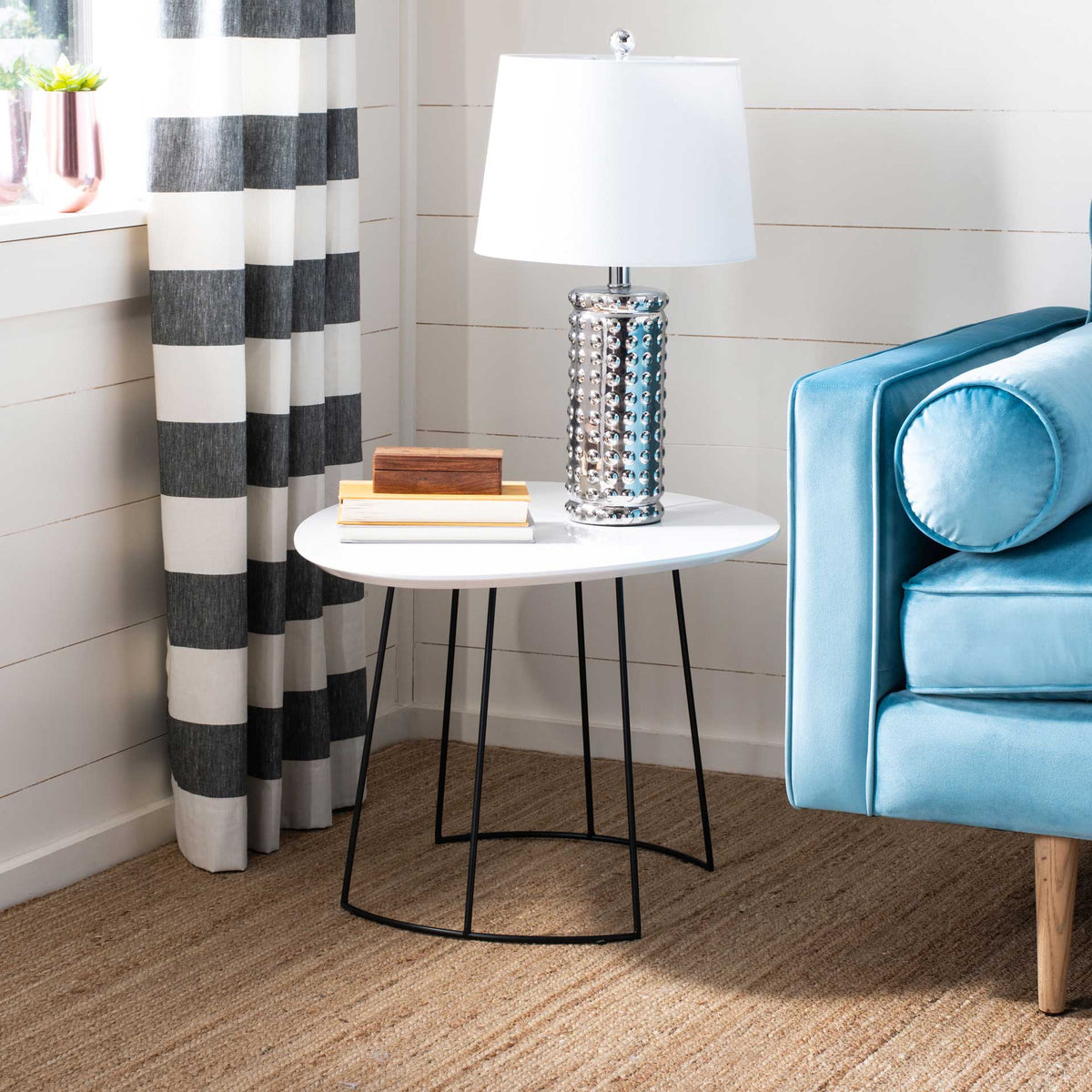 A white tabletop holds books and a lamp over an airy black iron base.