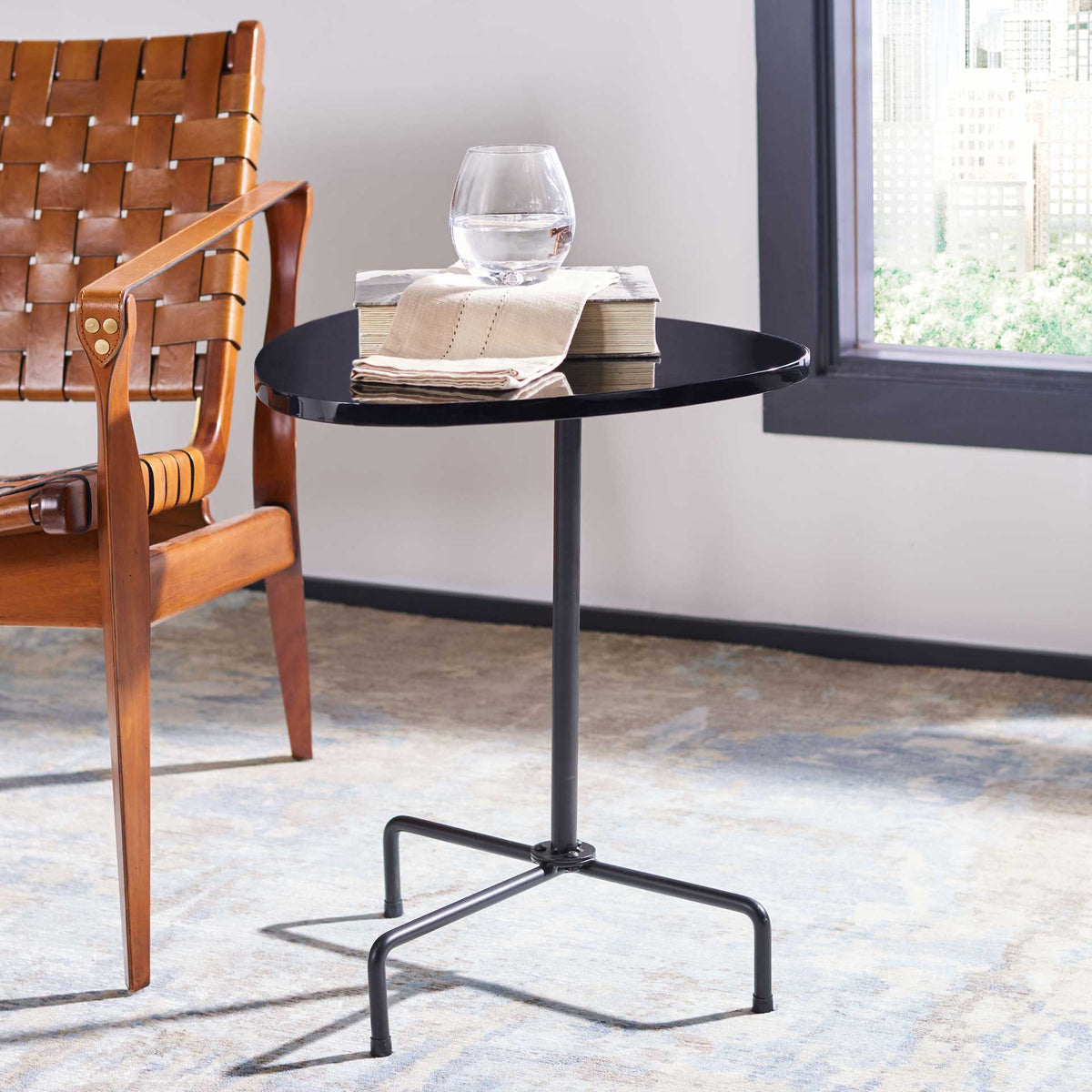 Books and a glass rest on the glossy black top above slim tripod legs.