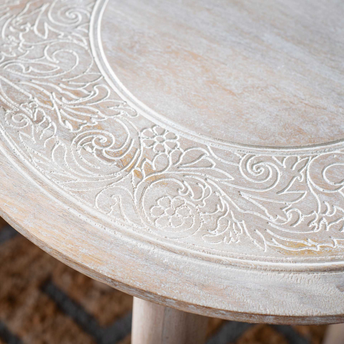 Floral scrollwork and raised whitewashed lines create rich texture around the tabletop.