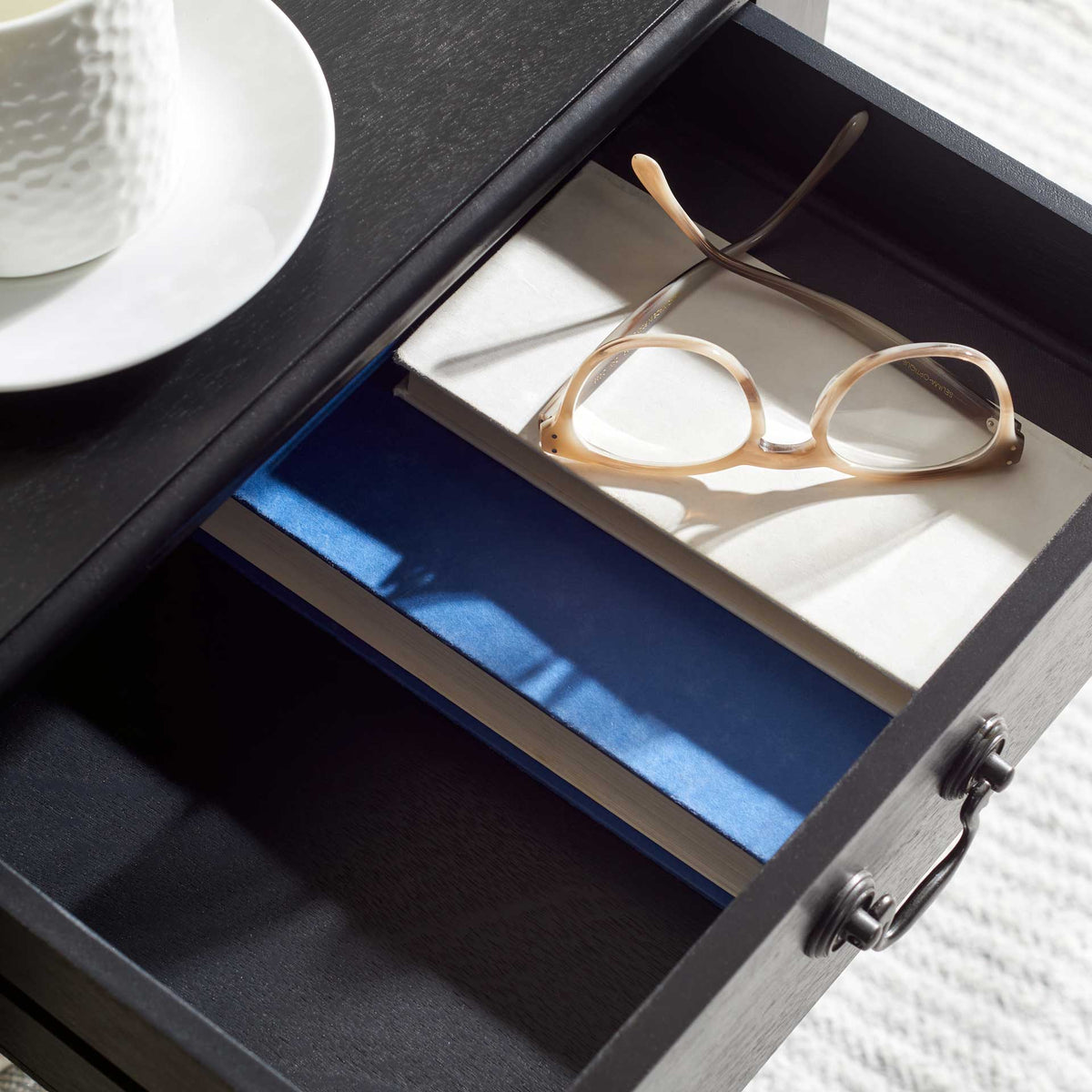The open black drawer holds glasses and books within easy reach beneath the tabletop