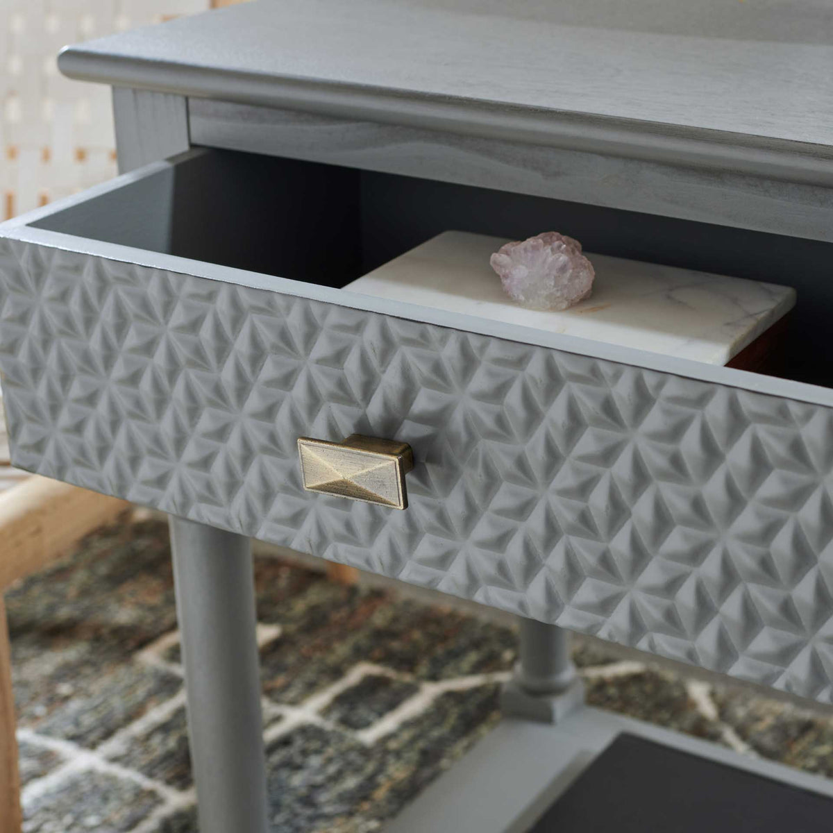 The embossed geometric drawer opens to reveal storage beneath the gray tabletop