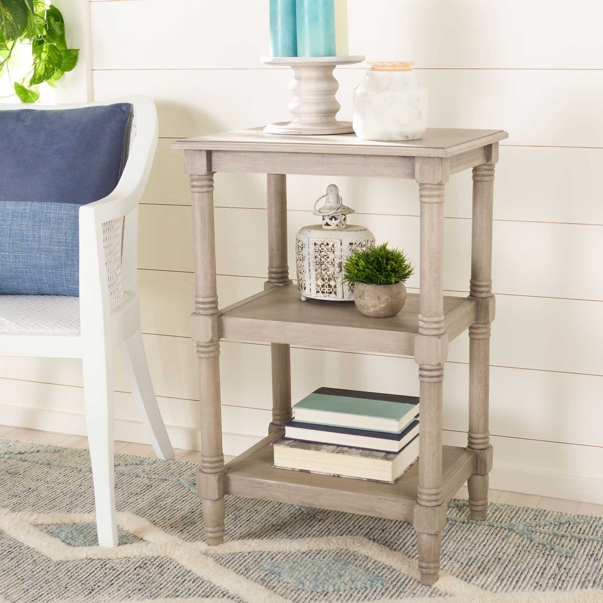 Pale greige table displays candles, greenery, and books on its open tiers.