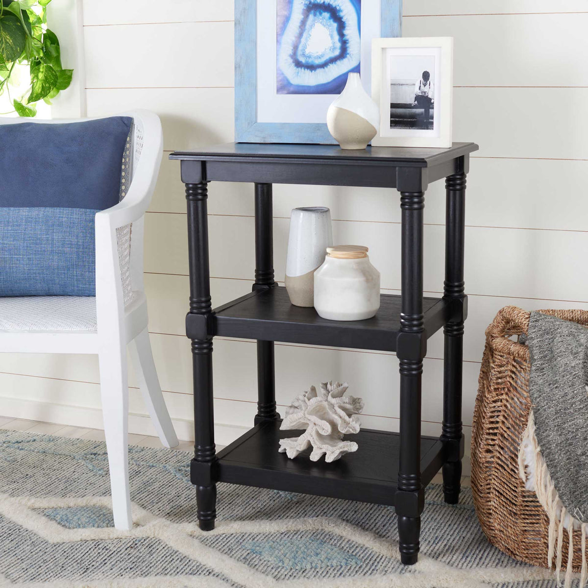 Black three-tier accent table holds decor beside a chair in a bright room.