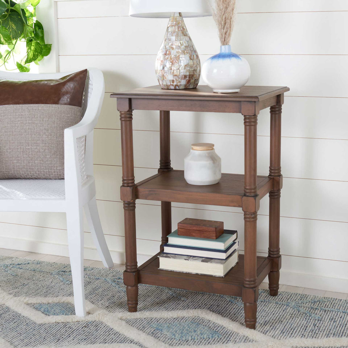 Warm brown table displays a lamp, vase, and books across its open tiers.