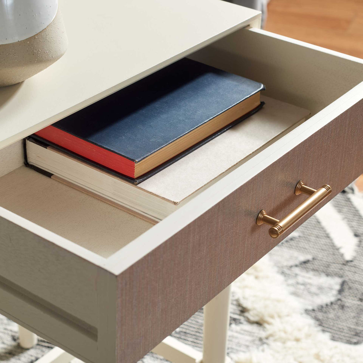 An open drawer offers space for books beneath a white tabletop, with a gold pull on its textured front.