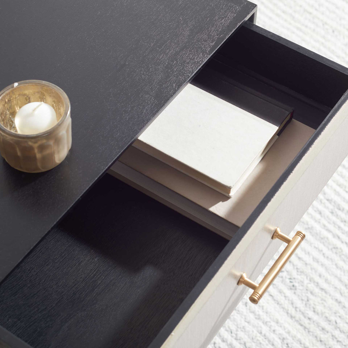 An open drawer holds books beneath the black tabletop, with a gold pull on its textured front.