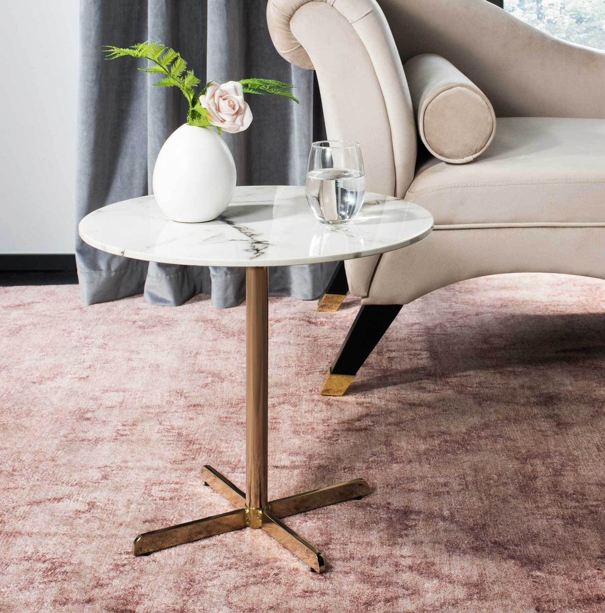 A marble-look round side table pairs a crisp white surface with a warm brass base beside a chair.