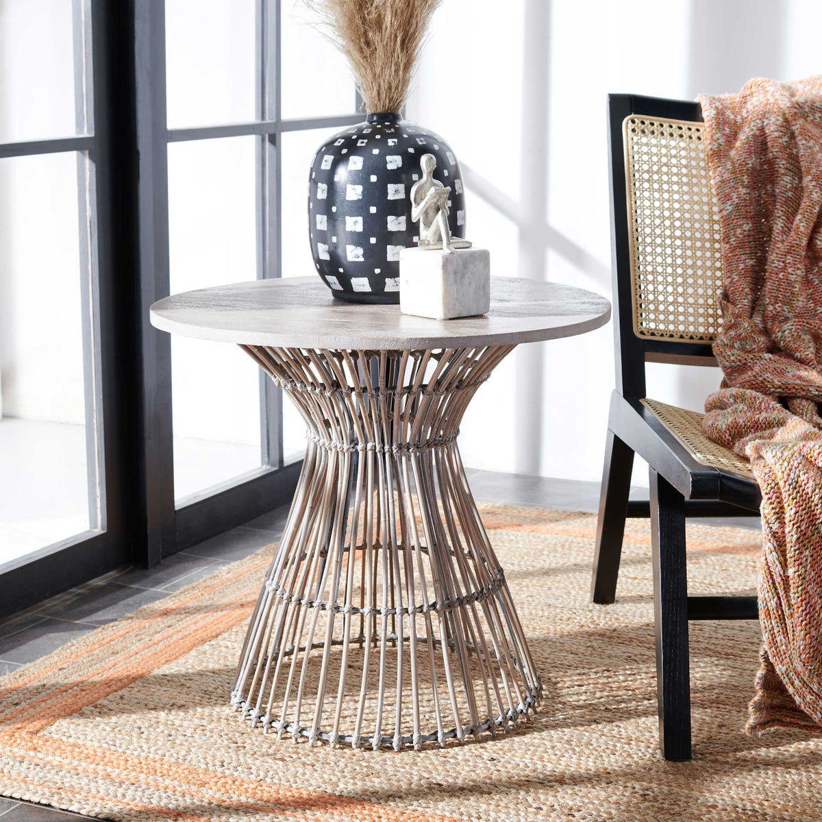The gray round table's open rattan base adds relaxed coastal texture beside a chair.