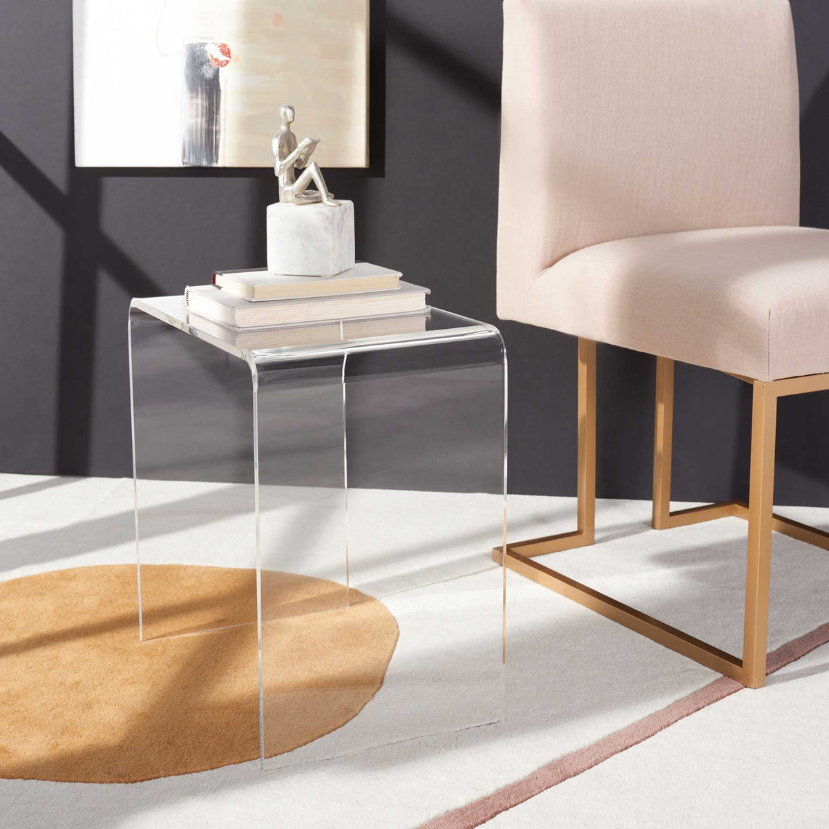 Clear acrylic side table displays books and decor beside an upholstered chair