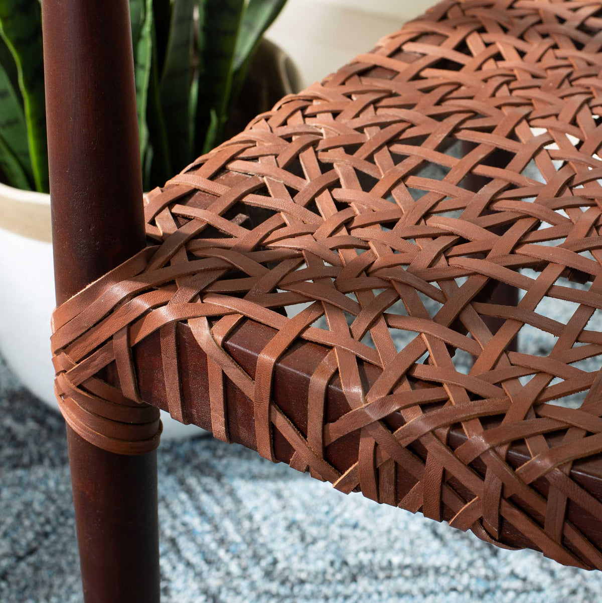 Brown leather strands crisscross over the seat and wrap snugly around the wood frame.