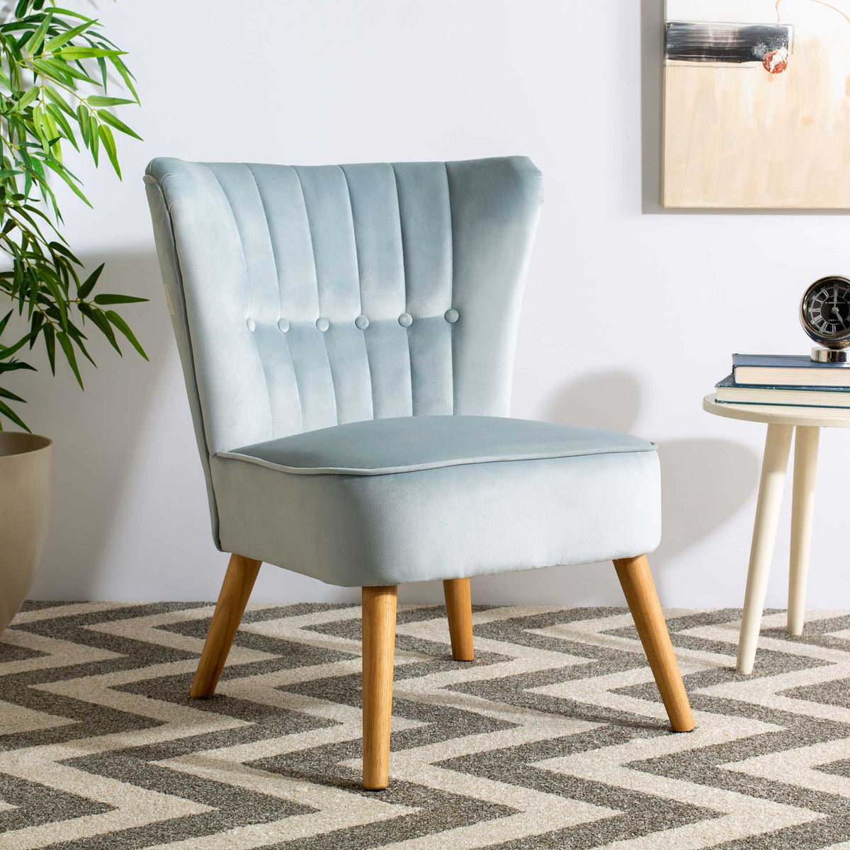 Slate blue velvet and natural wood legs complement a flared back with vertical tufting and buttons