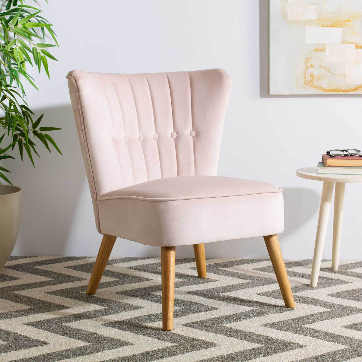 A pale pink velvet chair pairs a button-tufted back with a plush seat and natural wood legs