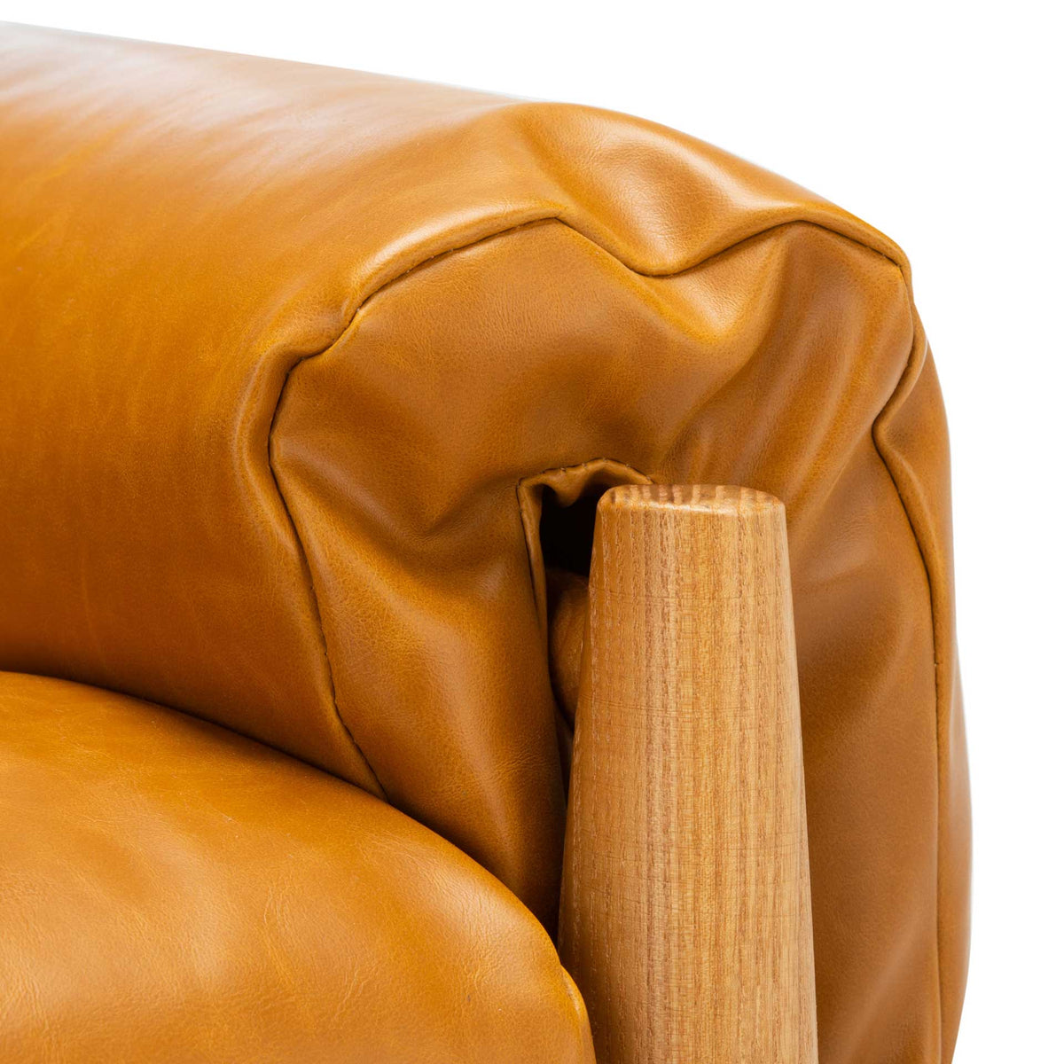 Gathered caramel upholstery wraps the rounded arm beside a natural oak post.