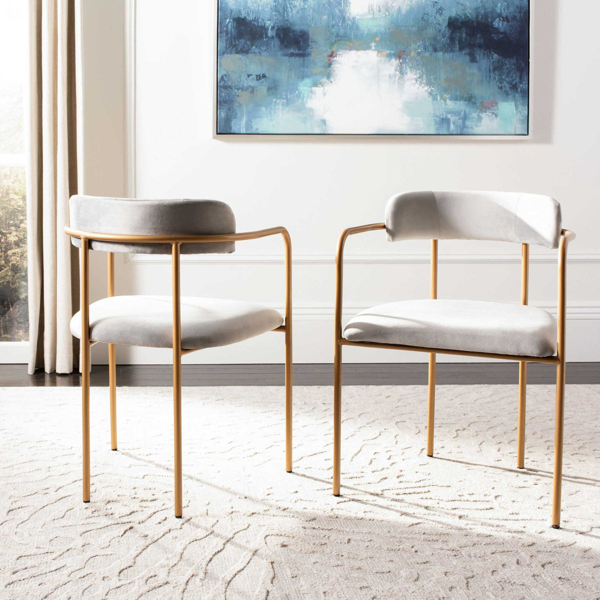 A pair of gray velvet chairs combines plush seats, curved backs, and gleaming gold frames