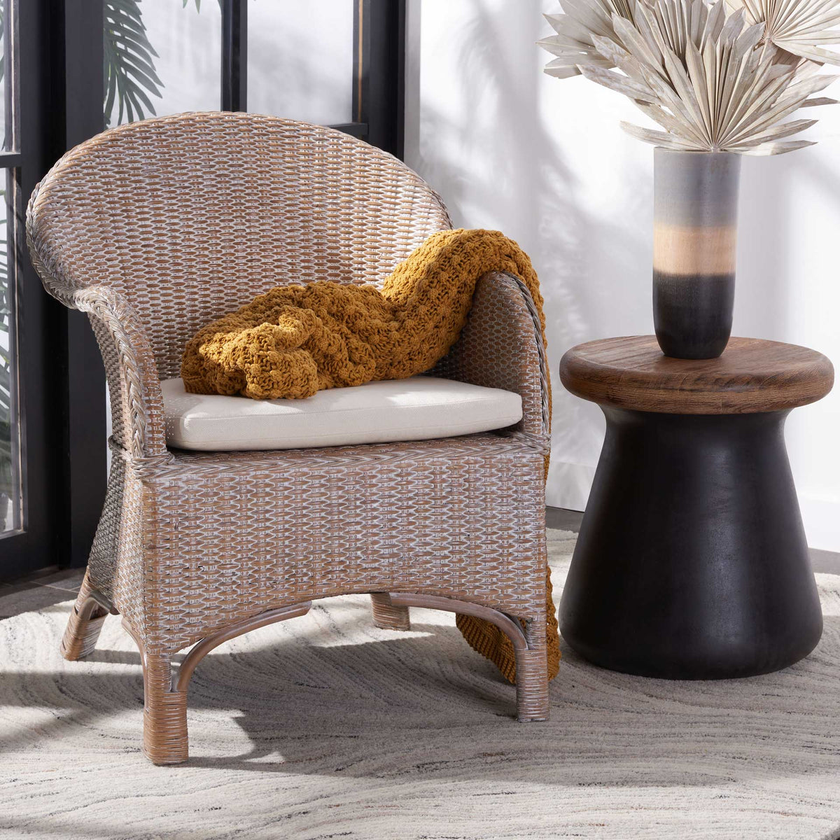 A whitewashed rattan chair pairs a sweeping back and white cushion for an inviting coastal touch.