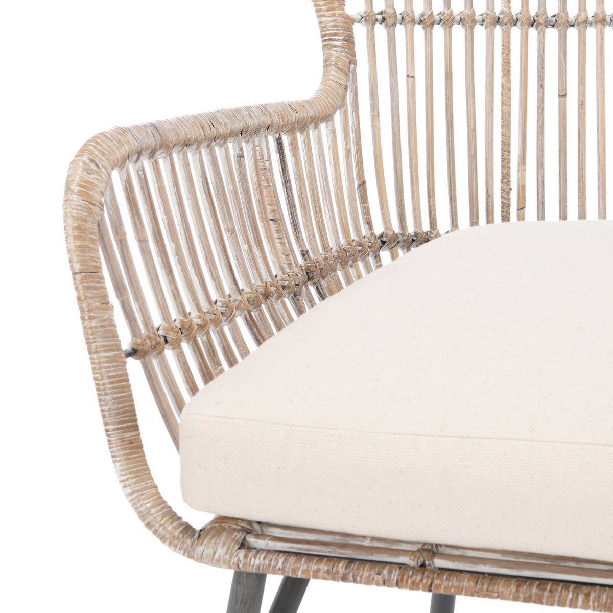 A thick white cushion nestles against a curved whitewashed rattan arm and wrapped seat edge