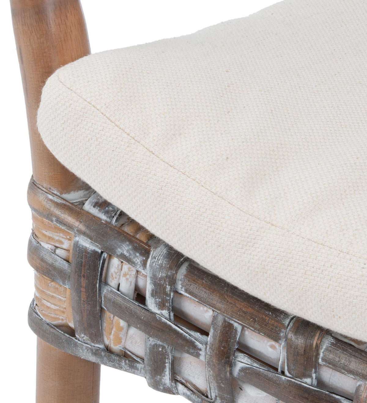 A soft white linen cushion sits atop woven rattan, with a rounded edge and warm wood support.