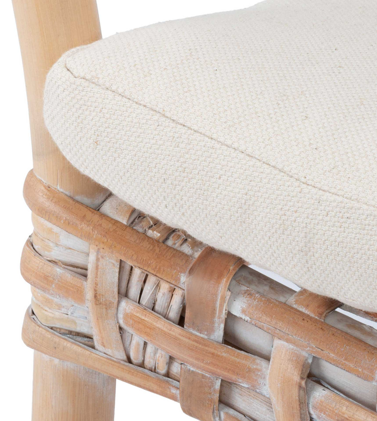 A white linen cushion rests against a pale woven rattan frame with a smoothly rounded edge.