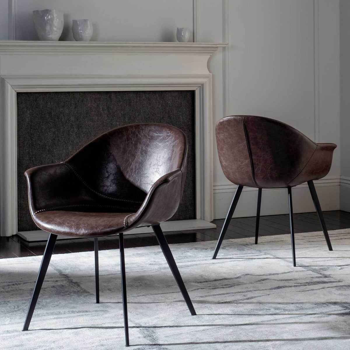Two dark brown faux leather tub chairs add sculptural curves and slim black metal legs to a living space.