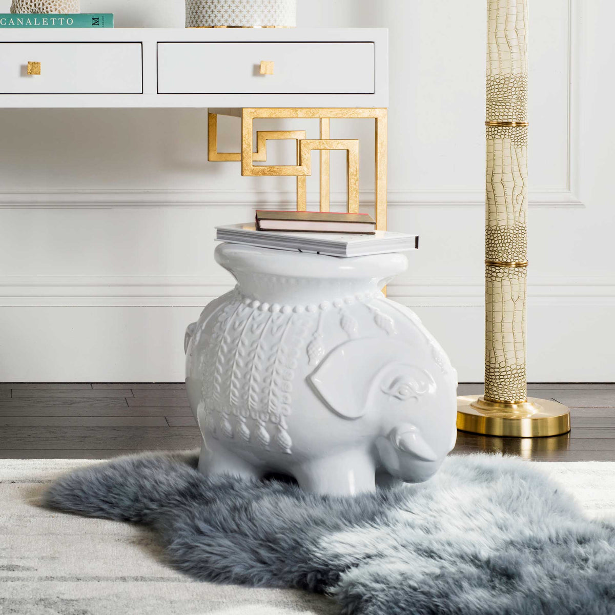 White elephant stool holds books near a gold-accented console and a soft gray rug.