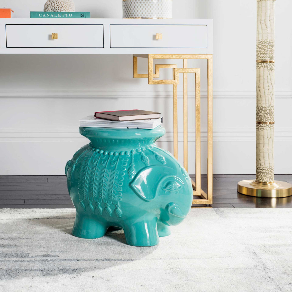 Robin's egg blue elephant stool provides a bright perch for books near a white console.