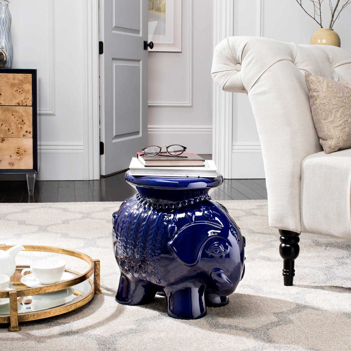 Navy elephant stool supports books and glasses next to a cream upholstered chair.