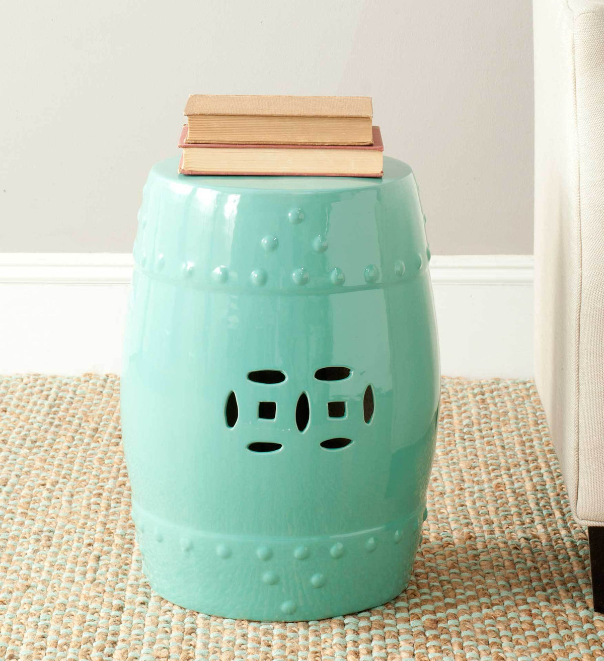 Light aqua stool with geometric cutouts serves as a colorful side table for stacked books.
