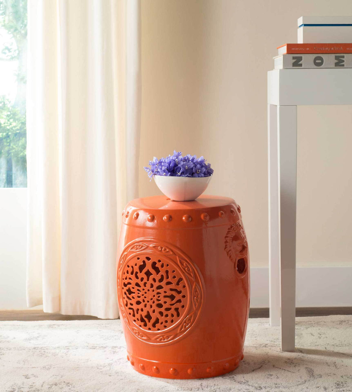 Bold orange garden stool doubles as a side table beneath a bowl of purple flowers