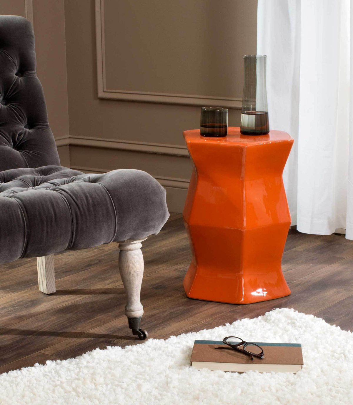 Bright orange stool works as a side table and adds sculptural color beside a tufted chair.