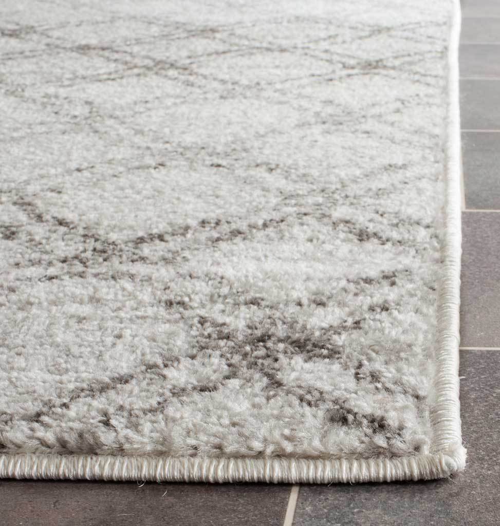 Soft silver pile and charcoal trellis lines meet at a neatly bound rug corner